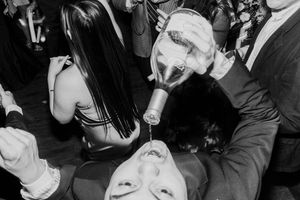 Black and white photo of wedding guest drinking from a funnel at a lively reception party.