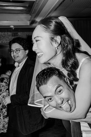 Black and white photo of laughing bride in veil and groom sticking out tongue at wedding.
