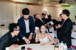 Bride reacts with delight during a magic card trick performance at wedding reception table.