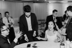 Black and white photo of magician performing card trick for bride at wedding reception table.