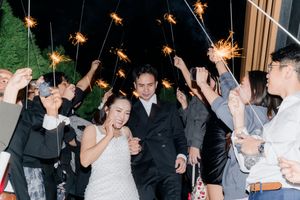 Bride and groom walking through sparkler send-off tunnel with cheering guests at night wedding.