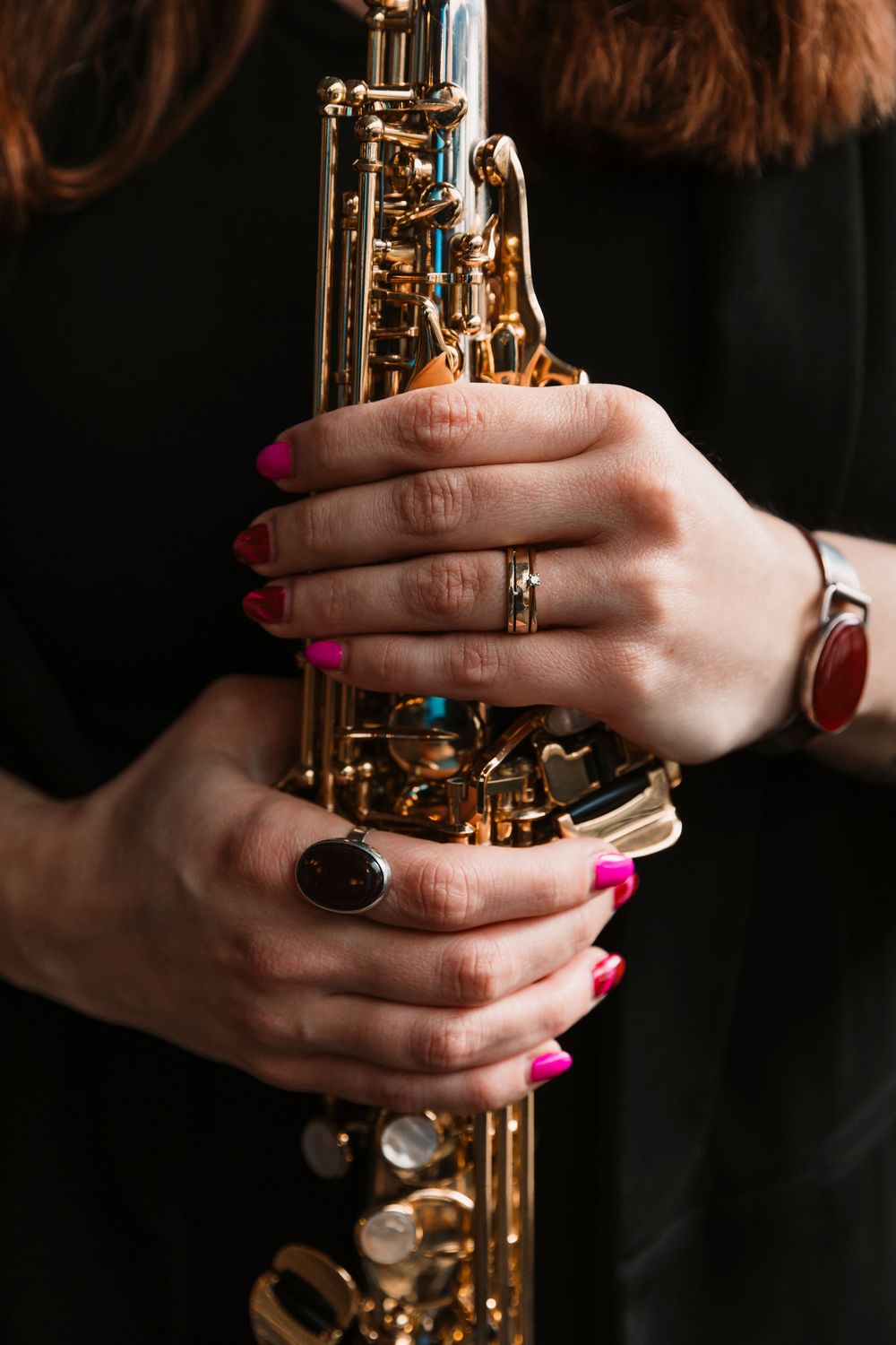 Close-up of hands with pink nails and rings holding golden saxophone.