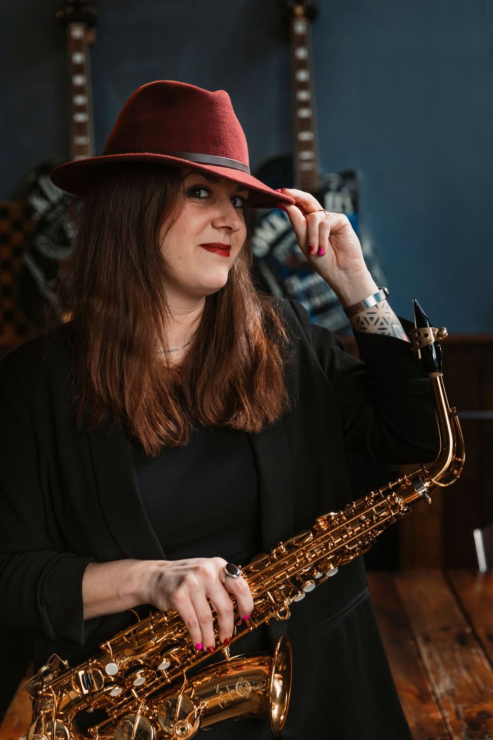 Musician in black attire and burgundy hat holding a saxophone in a moody indoor setting.