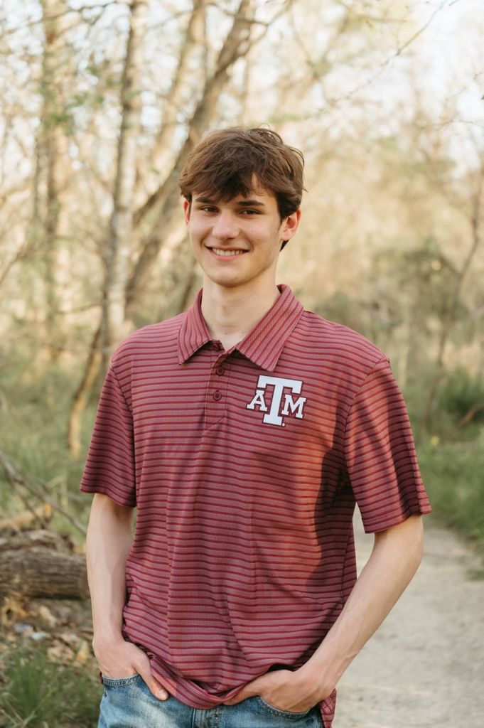 Smiling young man wearing Texas A&M striped polo shirt standing on outdoor trail.