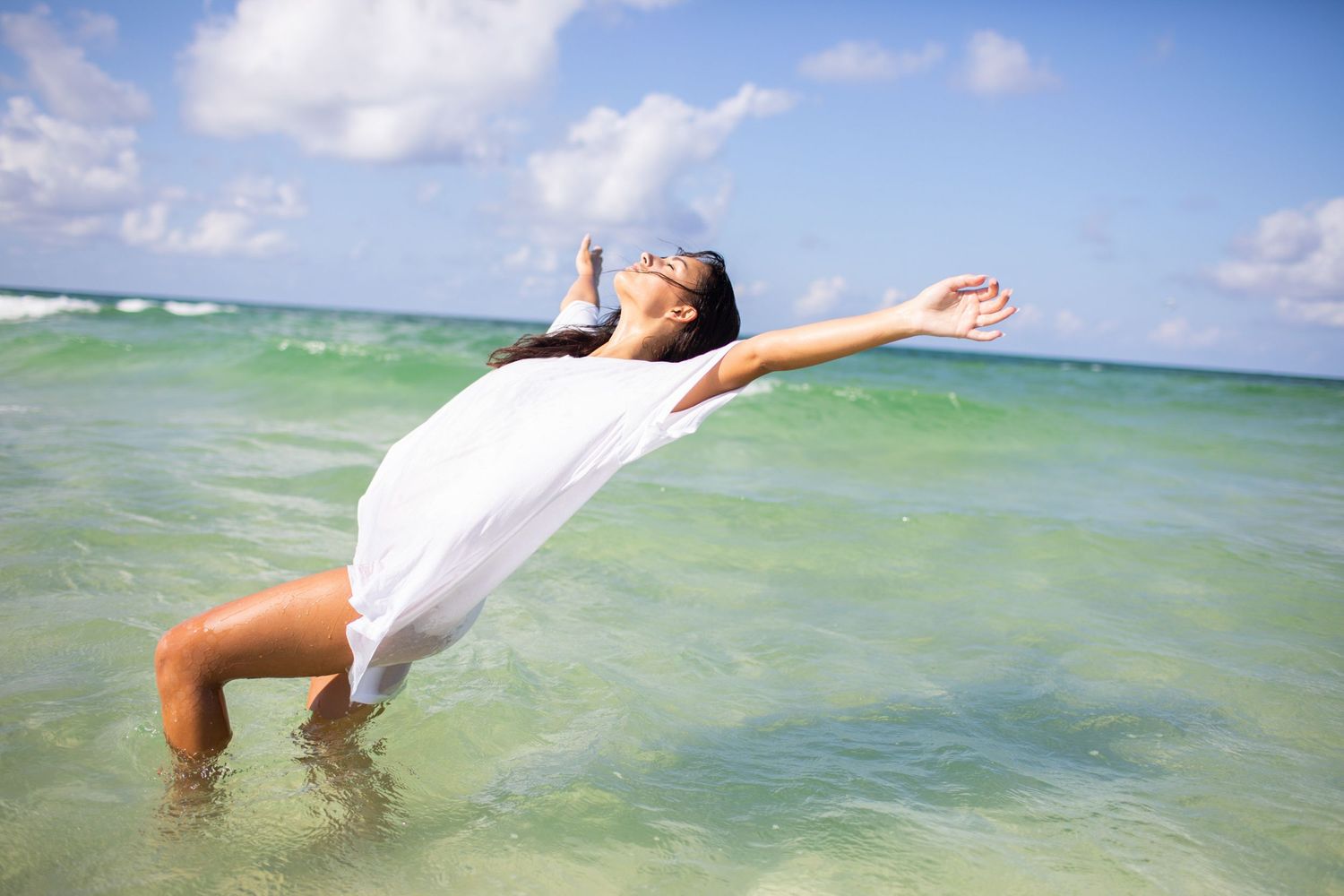 A person in white clothing dives gracefully into crystal clear turquoise ocean waters on a sunny day.
