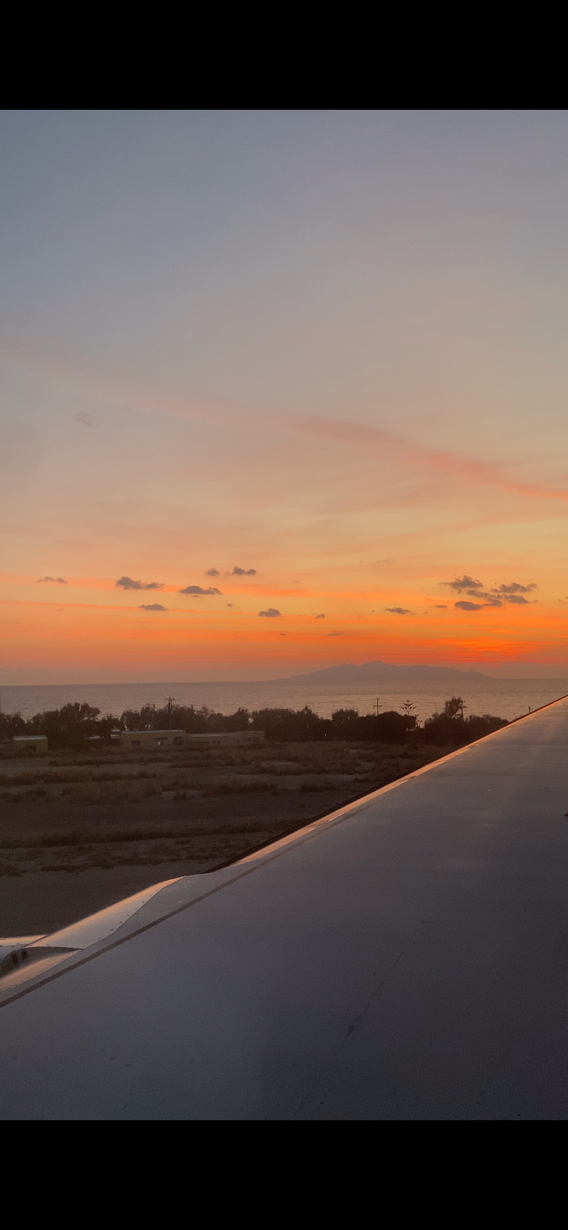 Sunset view from airplane window showing orange sky and dark wing silhouette against horizon.