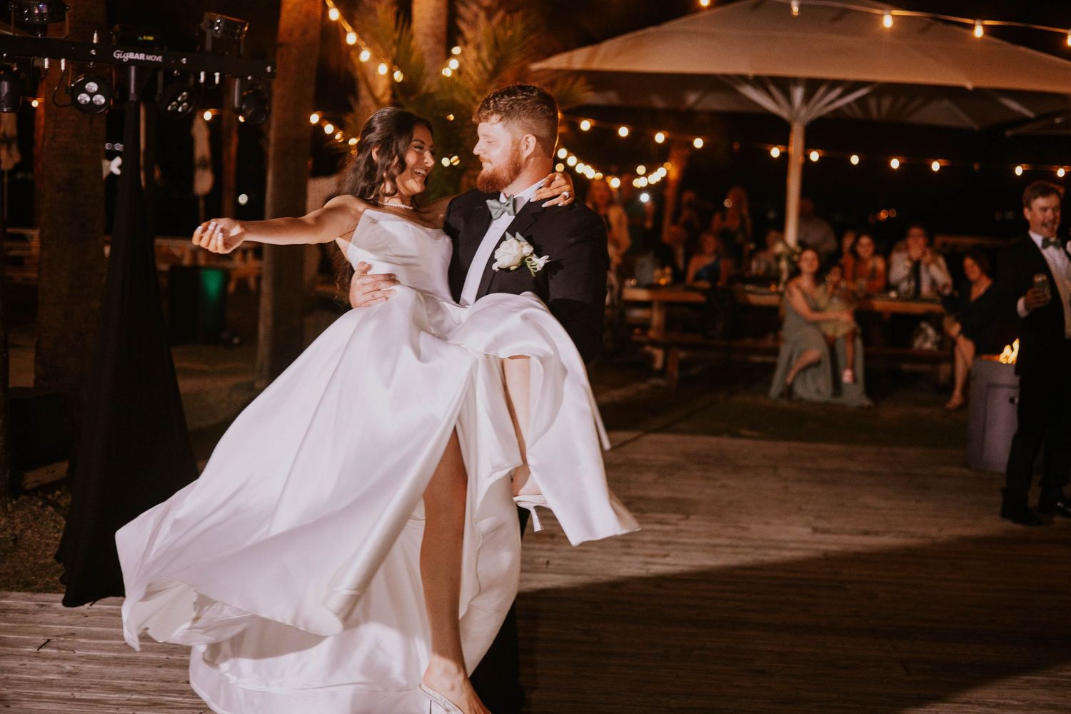 Couple dancing under string lights at an outdoor evening wedding reception.