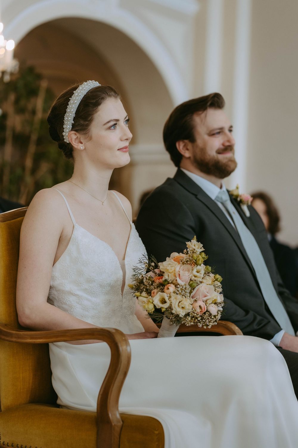 Couple sits together on antique yellow chairs during intimate wedding ceremony.