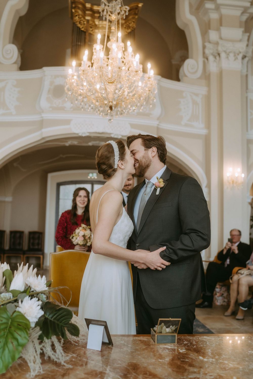 A couple shares an intimate moment during their wedding ceremony under an elegant crystal chandelier in a grand ballroom.