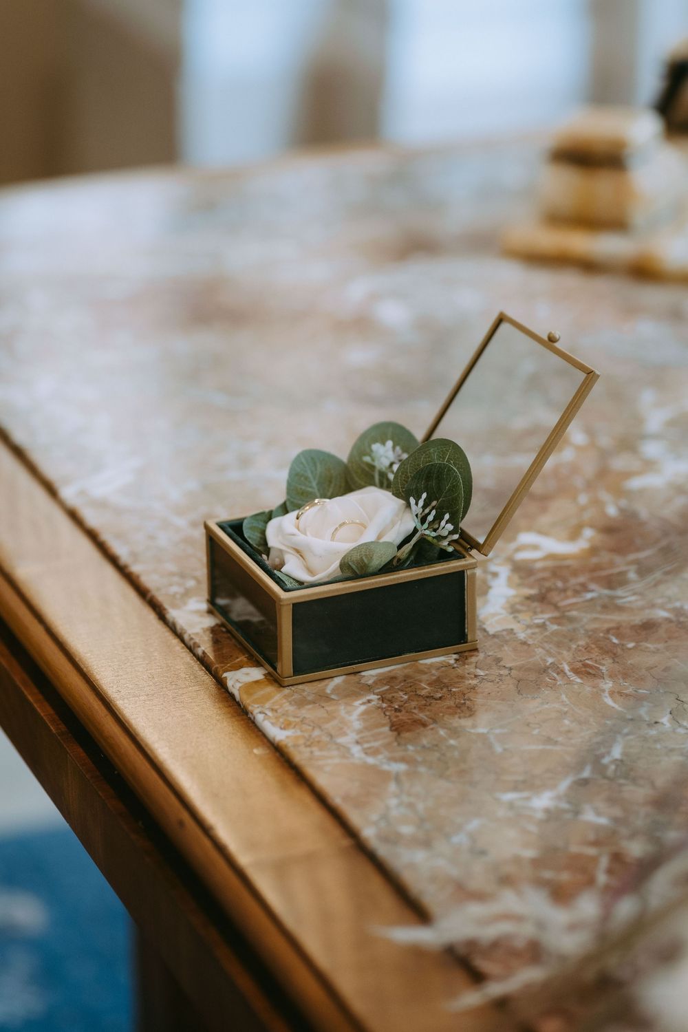 Close-up sequence of wooden ring box opening to reveal delicate jewelry on textured marble surface.