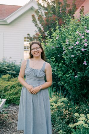 A gray summer dress is photographed in a garden setting with blooming flowers and greenery.