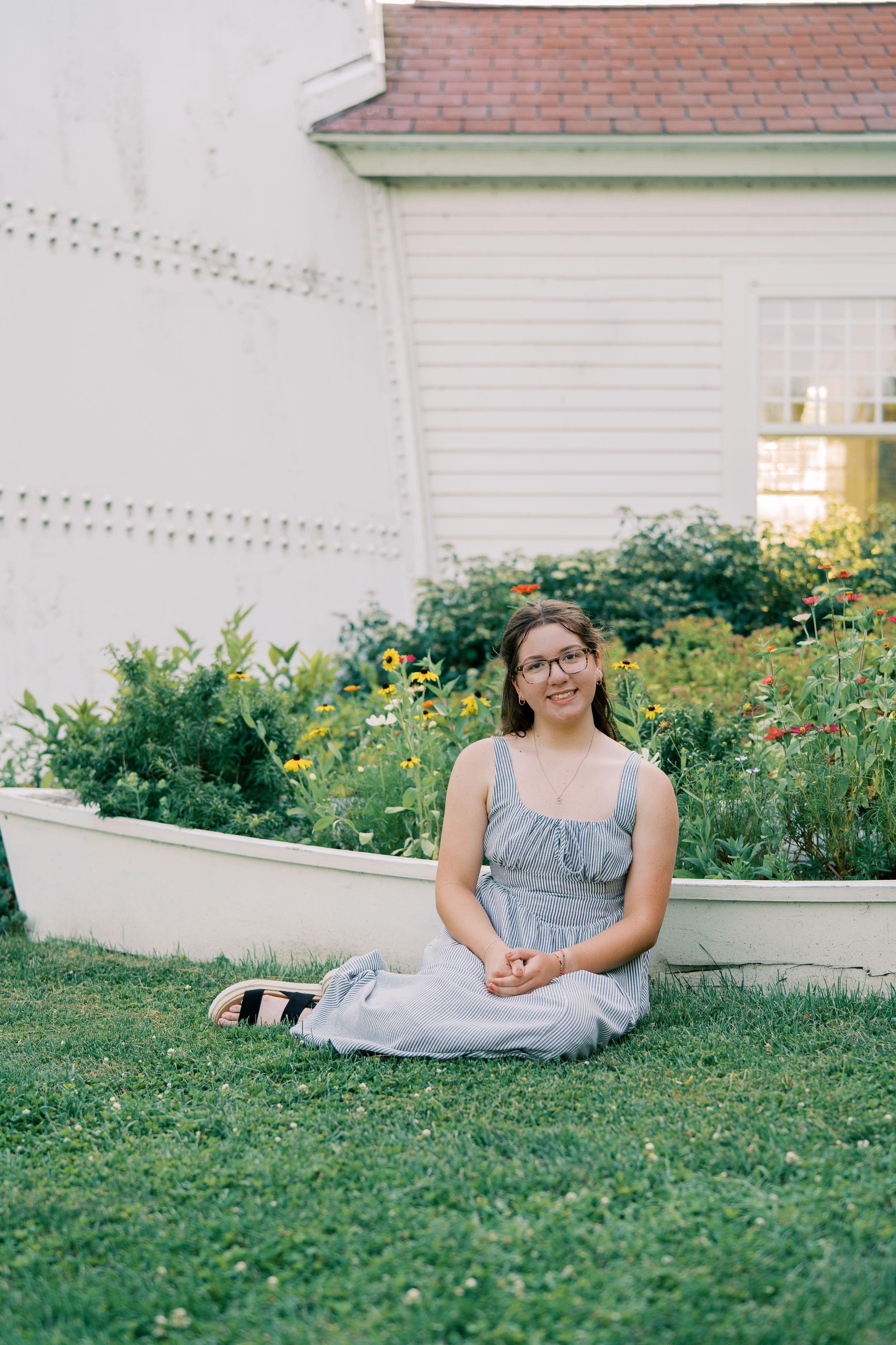 A gray striped dress is shown against a backdrop of lush summer gardens and white buildings.
