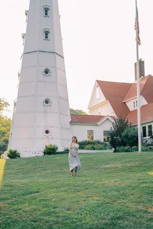 A white lighthouse tower stands tall against a blue sky with colonial buildings in the background.