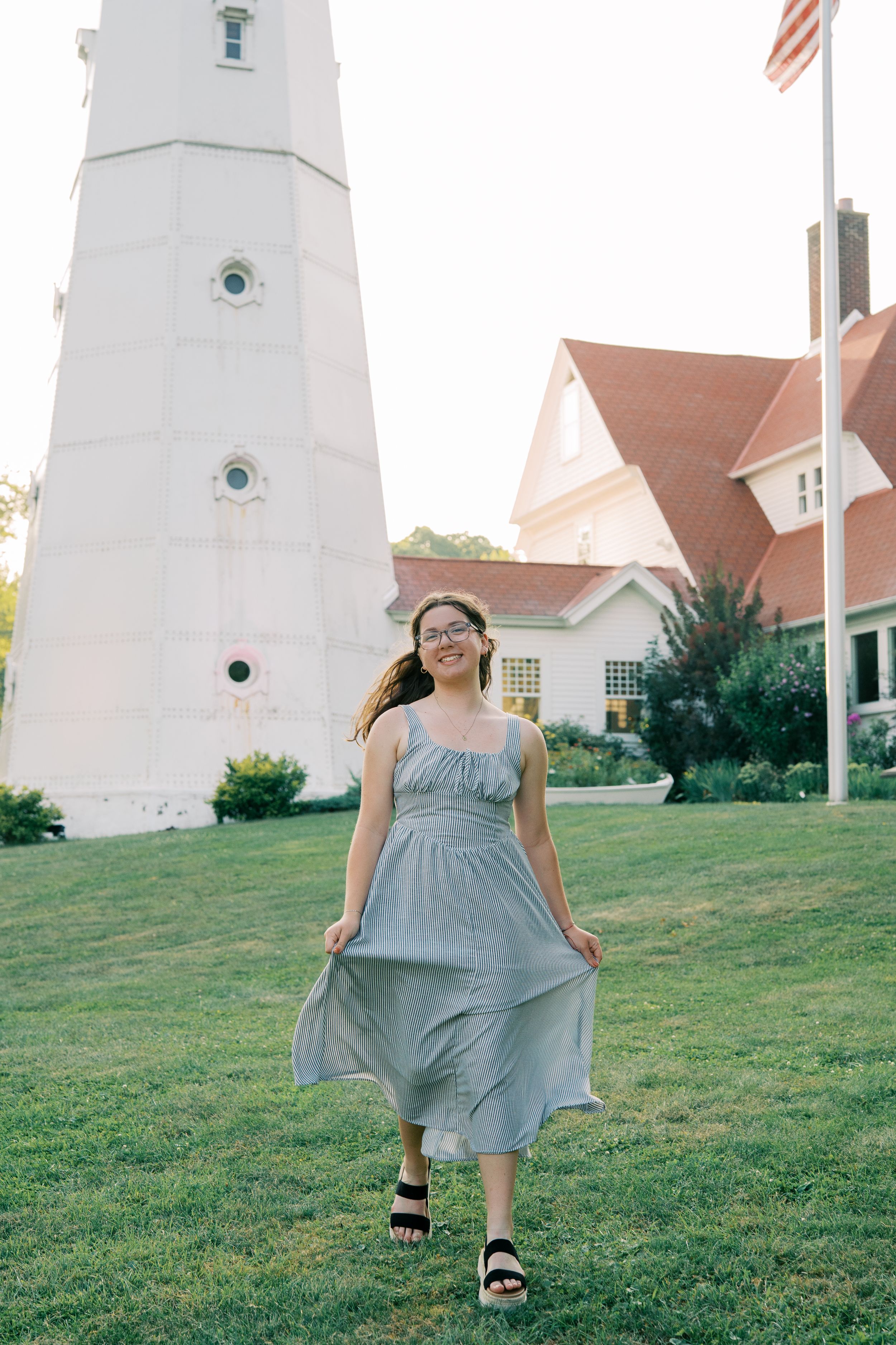A flowing gray dress twirls in front of a white lighthouse on a grassy hill.