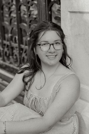 A black and white portrait of someone in a striped dress sitting by decorative ironwork.