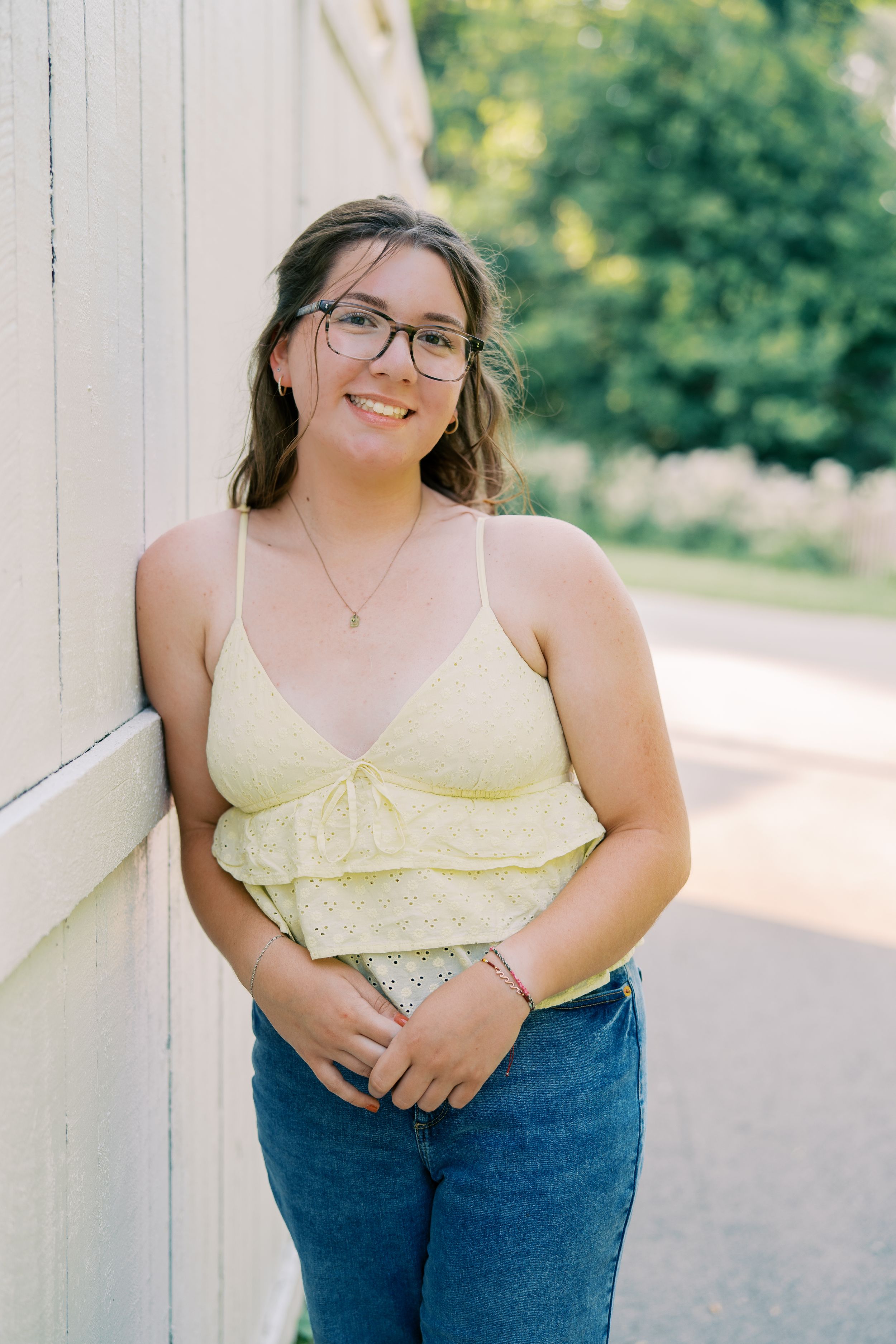 Summer portrait session against white wall wearing yellow top and denim.