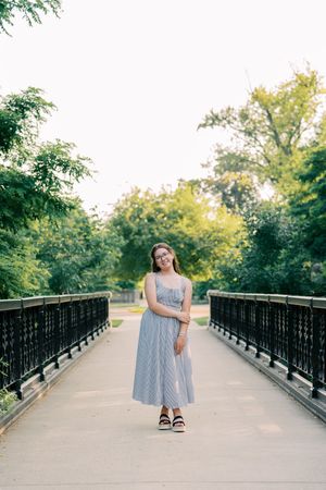 Summer portrait session on a bridge with black railings and green trees in background.