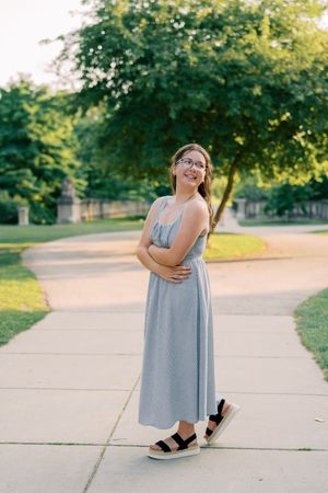 Full length portraits in a striped dress on a sunny pathway with trees.