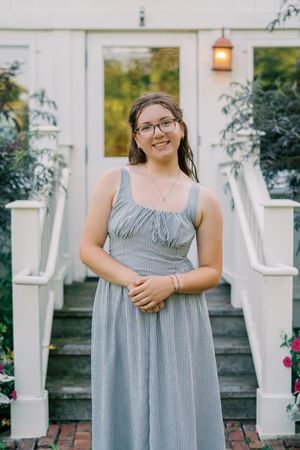 A striped gray sundress is worn on brick steps with white pillars and pink flowers in the background.