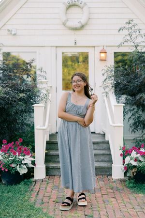 A gray dress is photographed against white porch columns with pink flowers and brick steps.