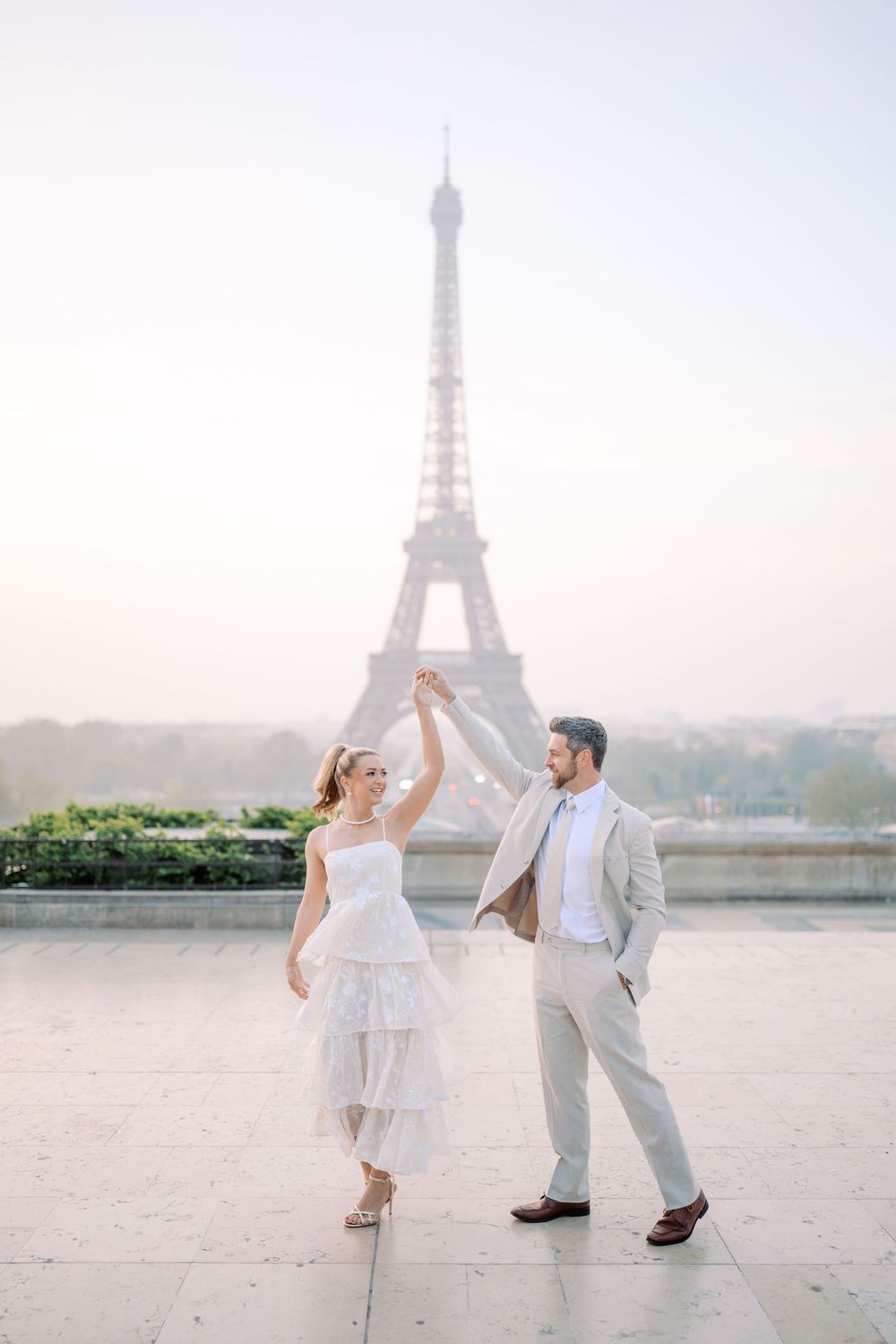 A couple dancing together in front of the Eiffel Tower on a misty morning in Paris.