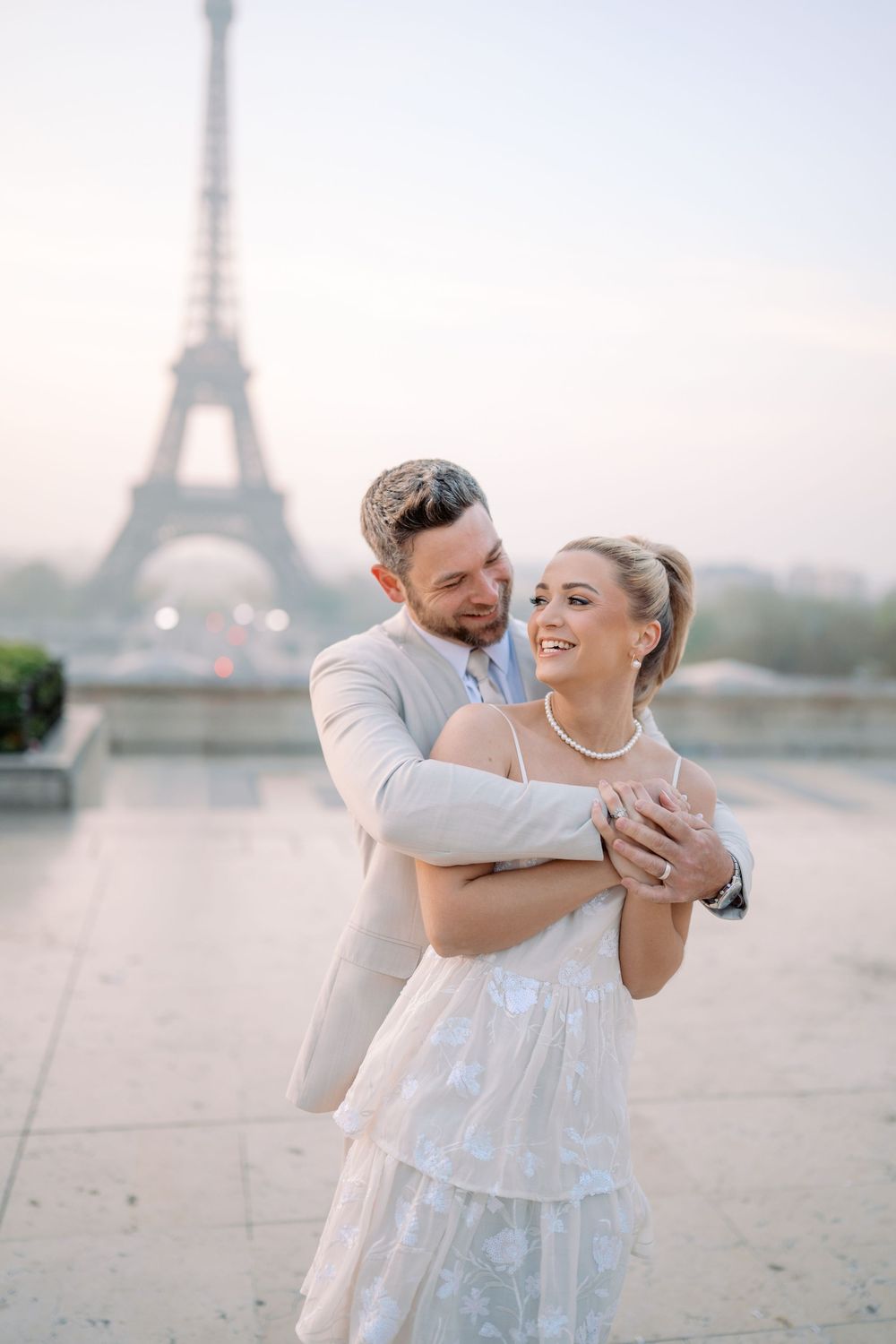 A romantic couple embraces in front of the Eiffel Tower in Paris during a dreamy sunset photoshoot.