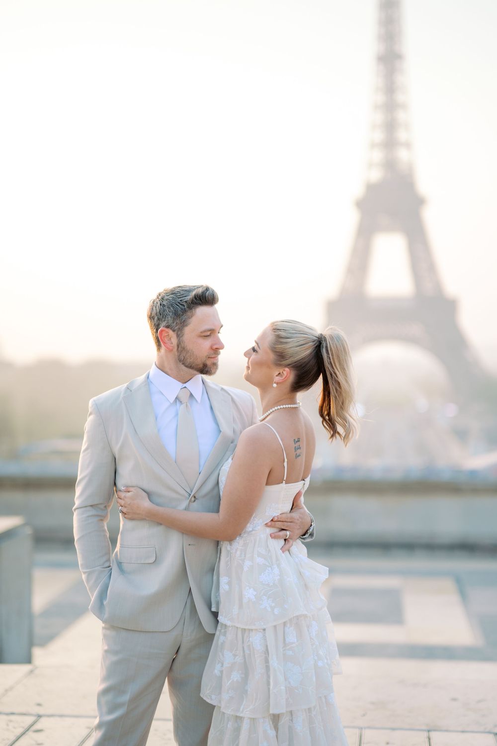 A romantic couple embracing in elegant attire with the iconic Eiffel Tower as their backdrop in Paris.