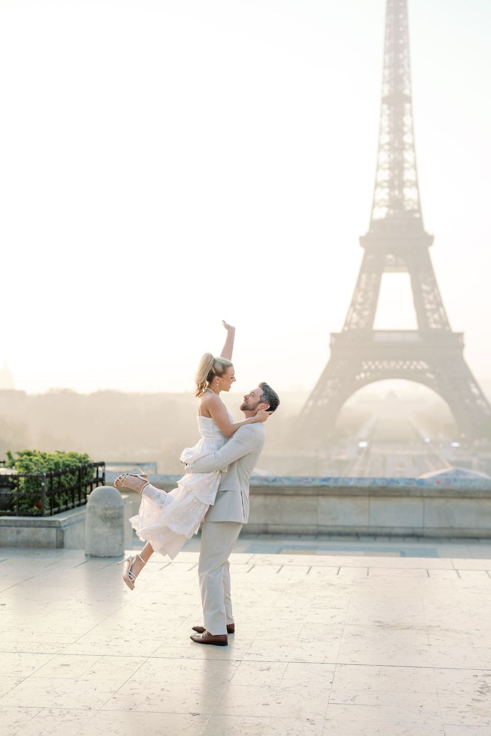 A romantic couple embraces in front of the Eiffel Tower in Paris during a misty morning photoshoot.