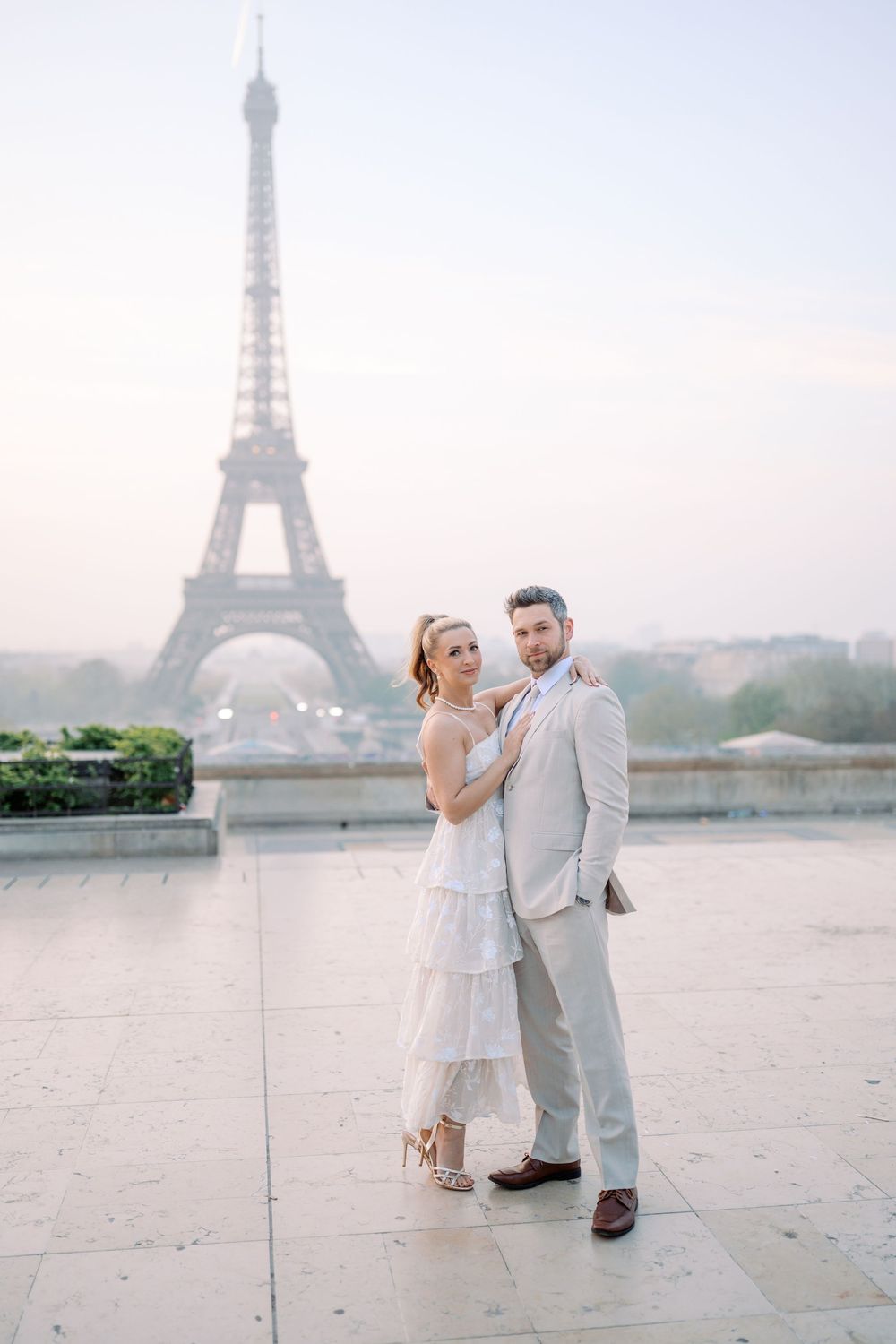 A couple poses together in front of the Eiffel Tower in Paris during a romantic photoshoot at sunset.