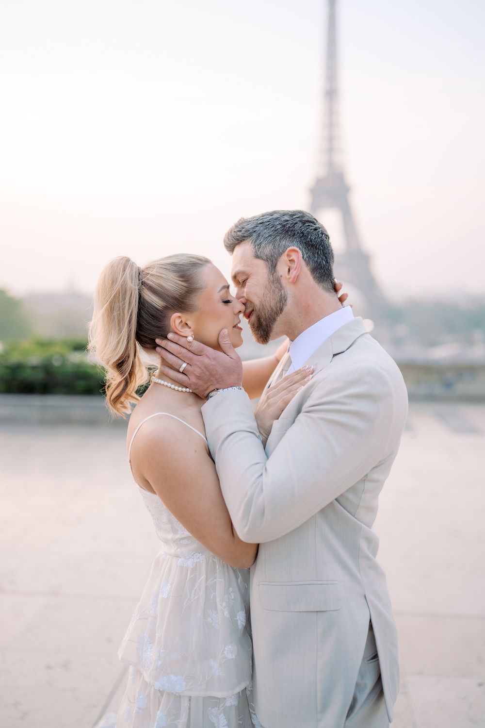 A romantic couple shares an intimate moment in front of the Eiffel Tower during sunrise in Paris.