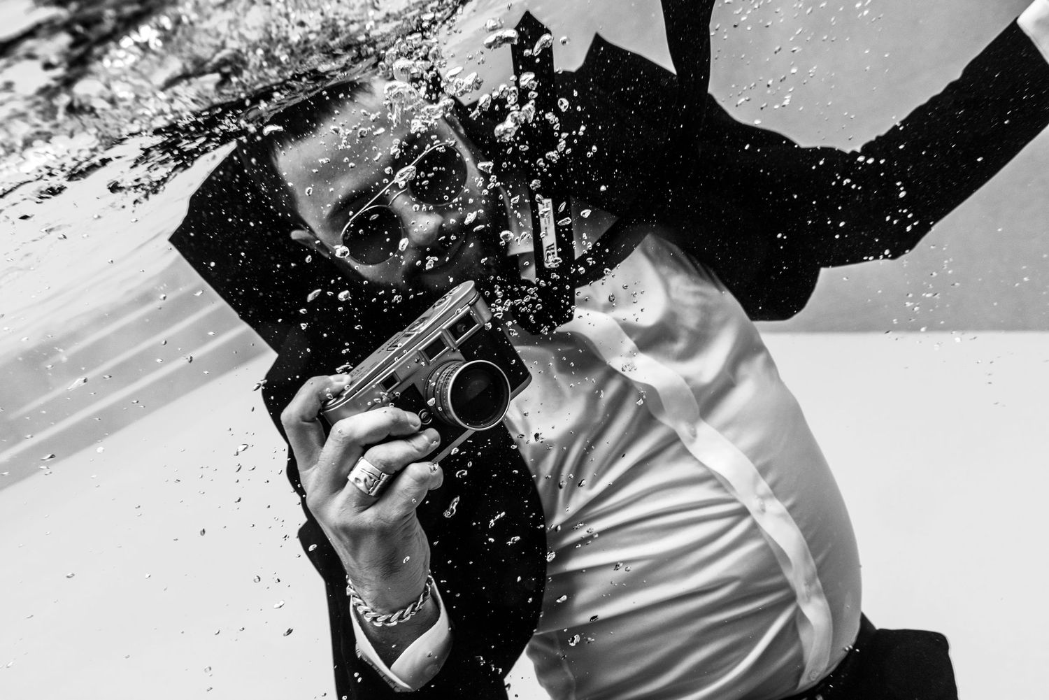 Black and white photo of a man in a suit holding a gun with dramatic water splash effect. From series Monochrome Night