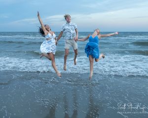 A group dances and plays at the beach during sunset, kicking up water and sand as waves crash on the shore.