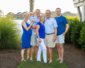 A group coordinated in blue and white casual attire poses together outdoors near coastal vegetation and water.