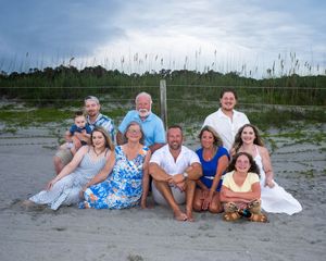 A group of people lounging together on a sandy beach at dusk wearing casual summer attire.