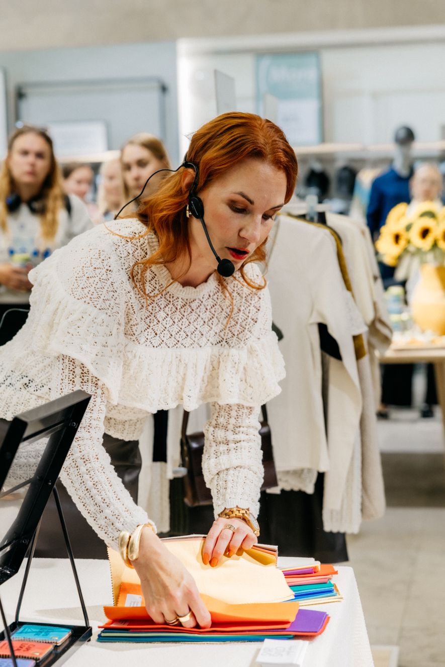 Designer in white lace blouse arranges colorful fabric swatches on table in fashion workspace.