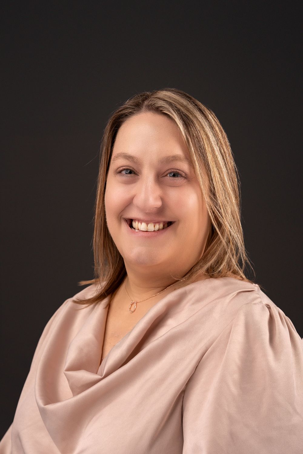 Professional headshot in soft pink top against dark studio background.