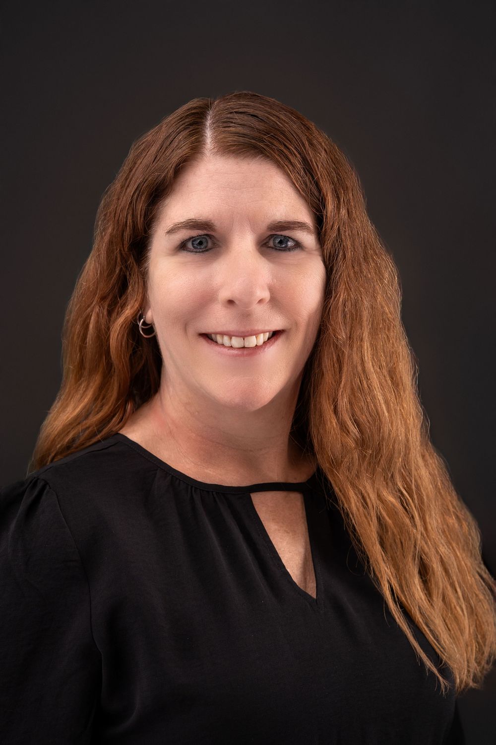 Studio portrait with long hair wearing black top against dark backdrop.