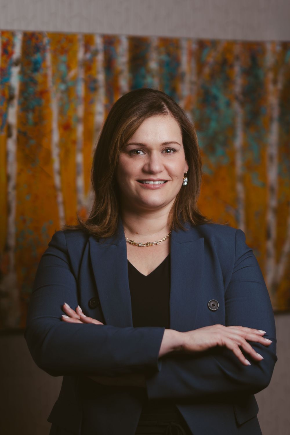 Professional headshot against rustic orange and teal backdrop wearing navy blazer and black top.