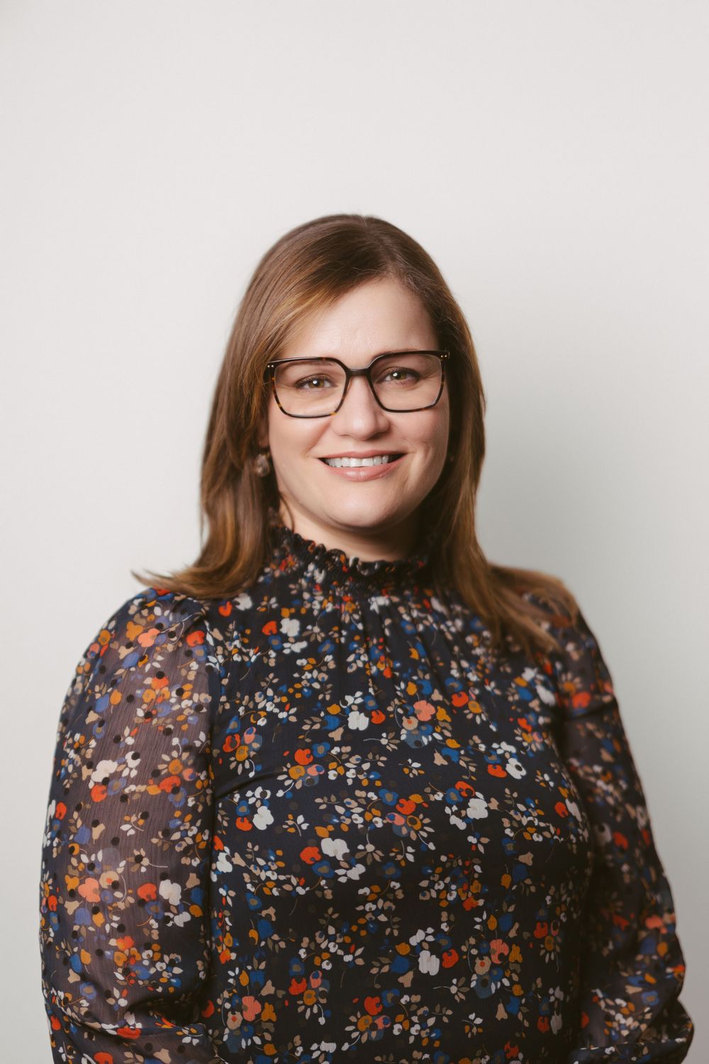 Studio portrait against white background wearing floral print top and glasses.