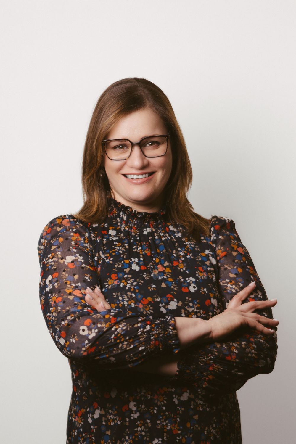 Professional poses in dark floral high-neck blouse against white backdrop.