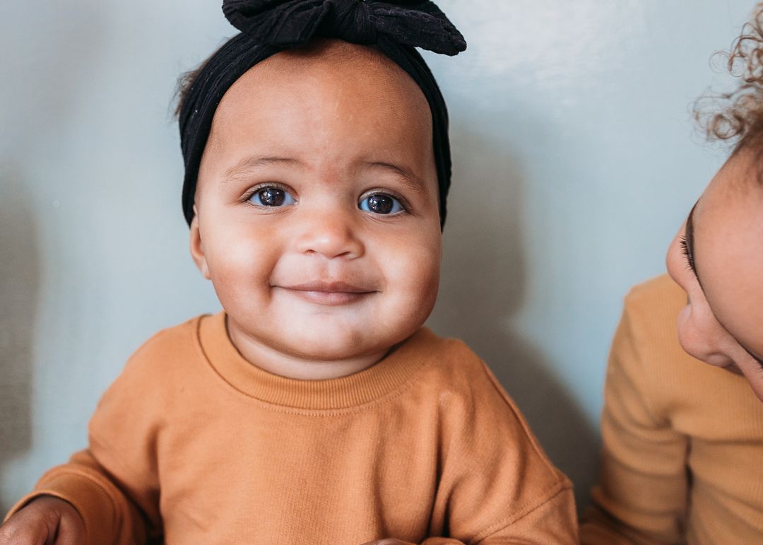 Baby wearing orange sweatshirt smiling and making playful expressions in a series of connected photos.
