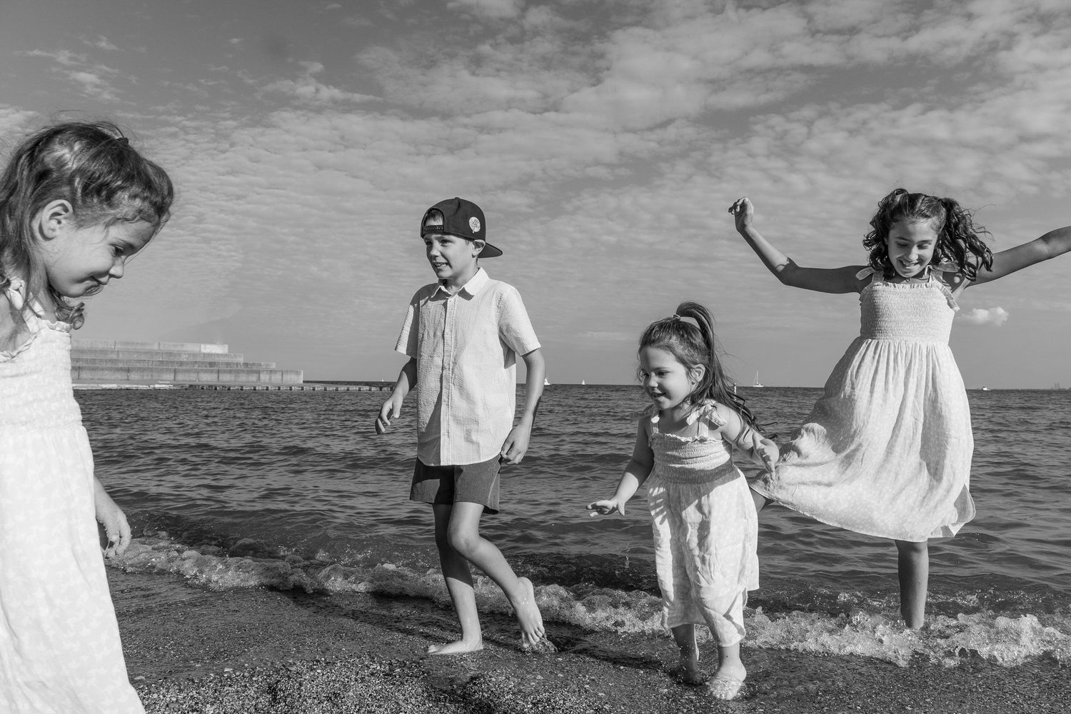 A black and white photograph of four young children playing on a beach.