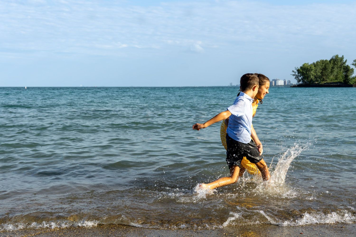 A young person running through the shallow water at the beach, creating splashes.