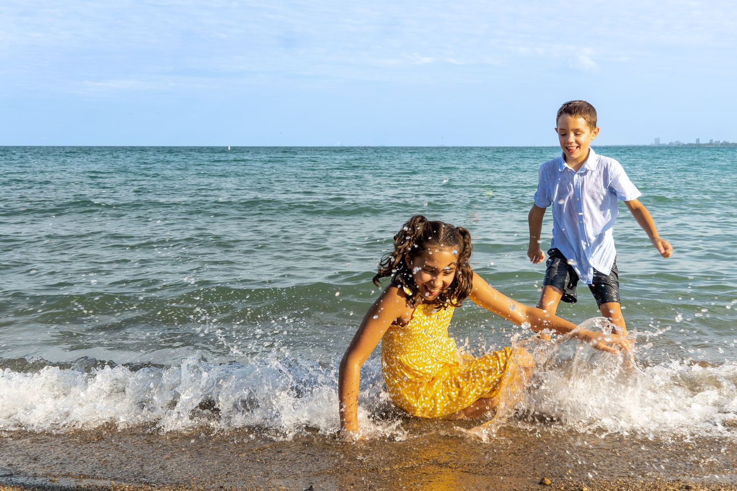 A young boy and girl playing in the waves on a beach.