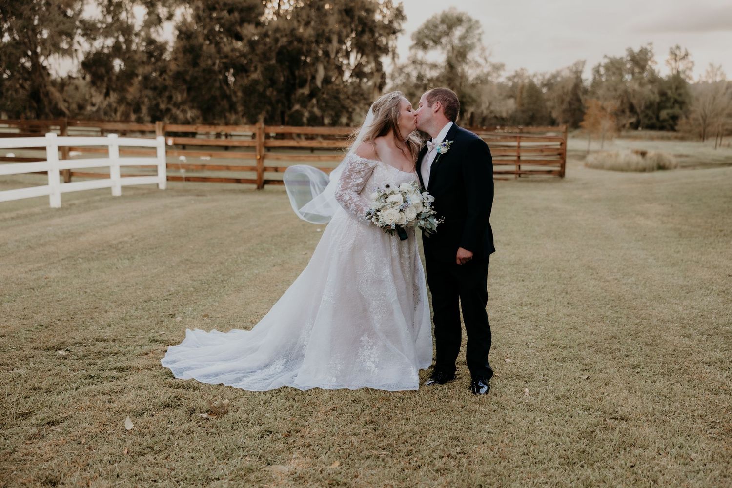 Bride and groom share a romantic moment outdoors at a farm wedding, bride wearing lace off-shoulder gown with veil.