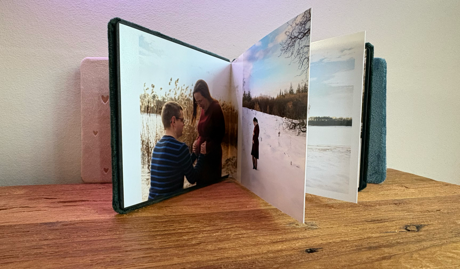 Open fotoalbum op houten ondergrond met romantische verlovingsfoto's van een stel in een besneeuwd winterlandschap. Harmonica boekje