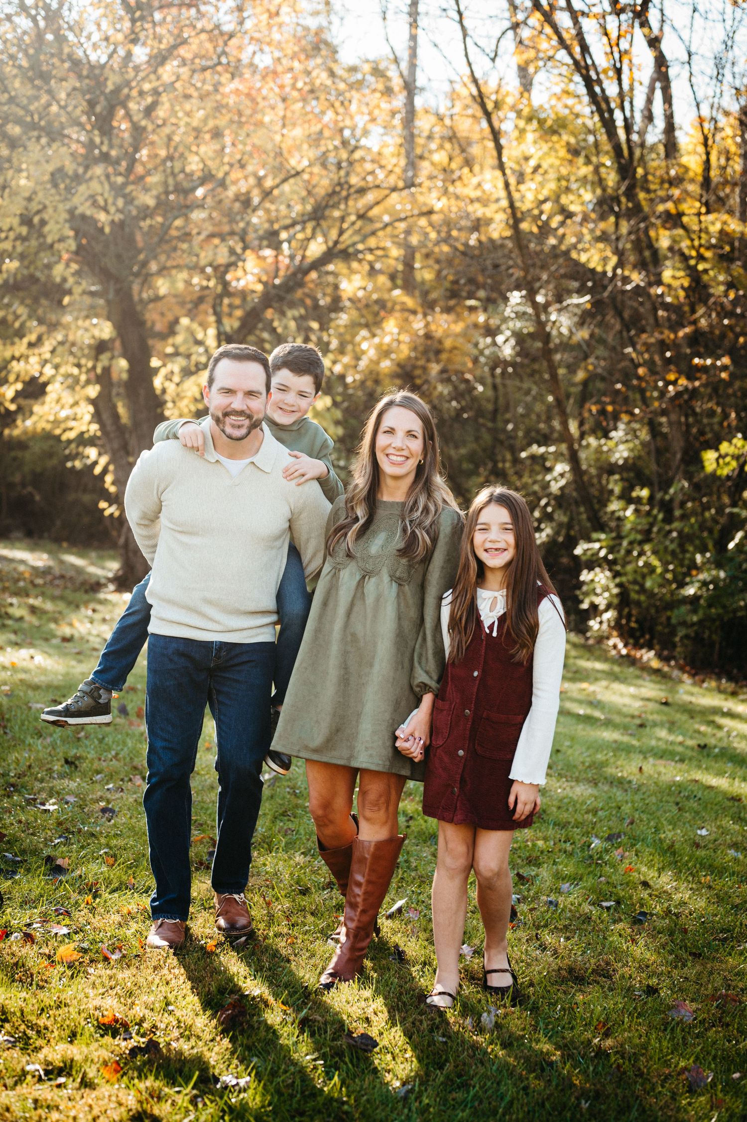 A family shares joyful moments together on a grassy hillside during golden hour in autumn.