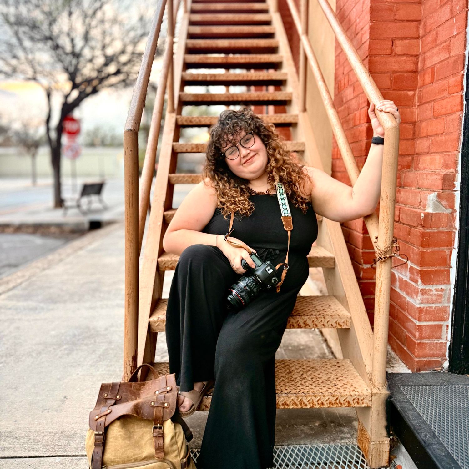 Jenna Bowman sitting on stairs with her camera and her camera bag at her feet in downtown Seguin Tx
