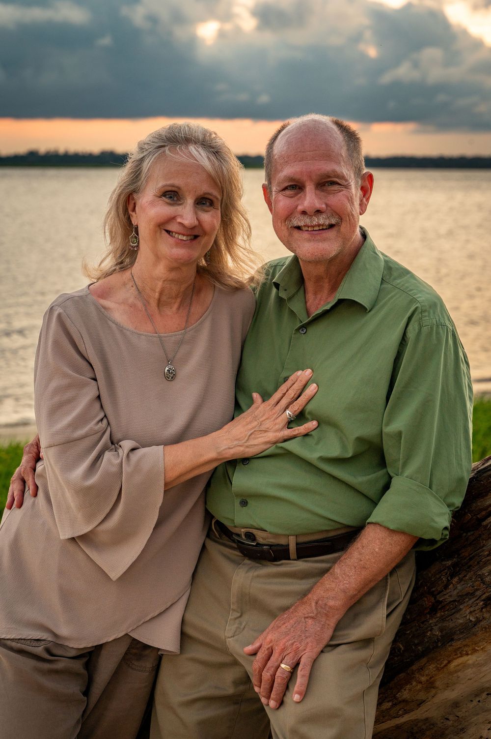 Senior couple shares tender moments at sunset by the waterfront in matching beige and green outfits.