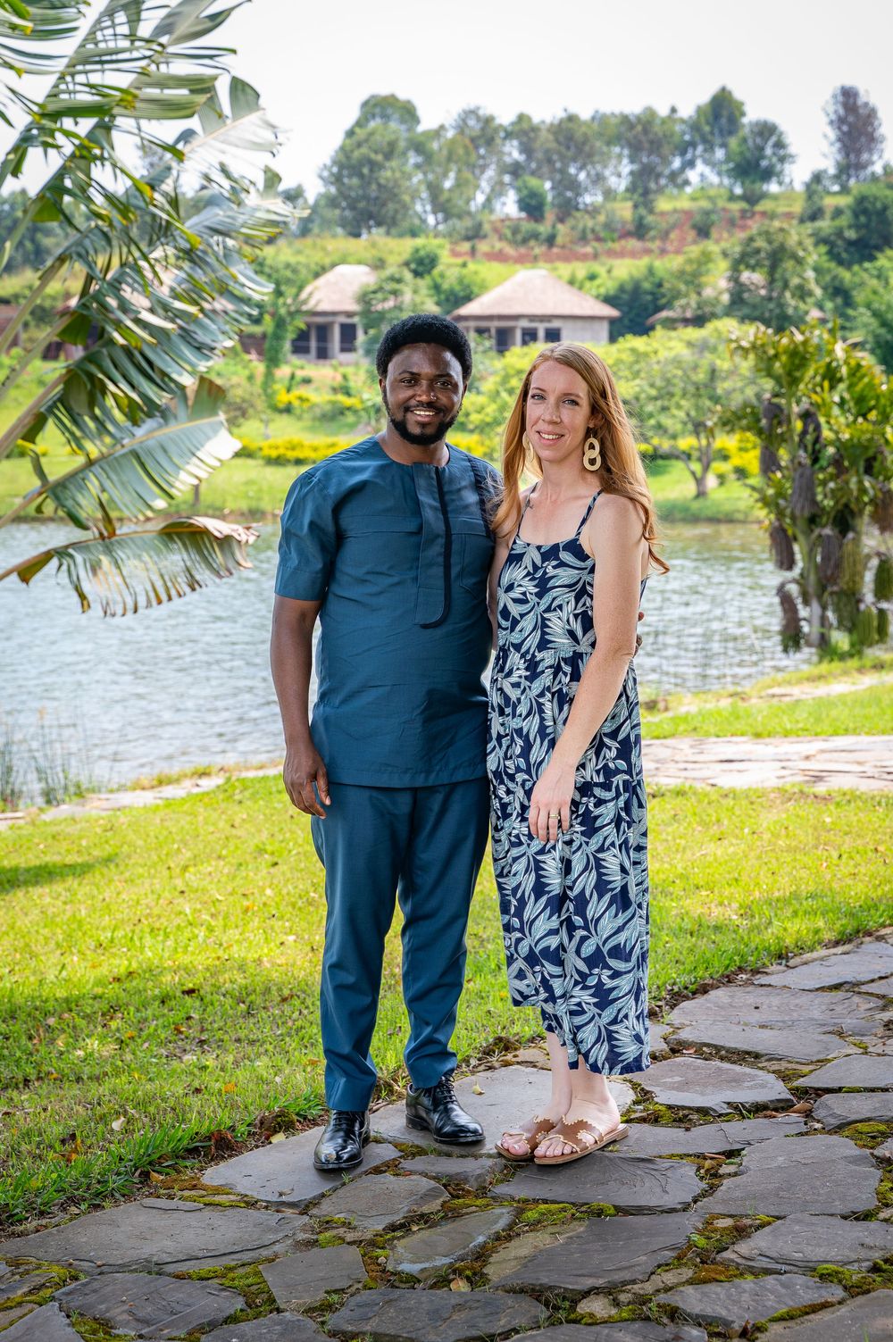 Couple poses together outdoors by a lake with palm trees and stone pathway in a romantic photoshoot series.